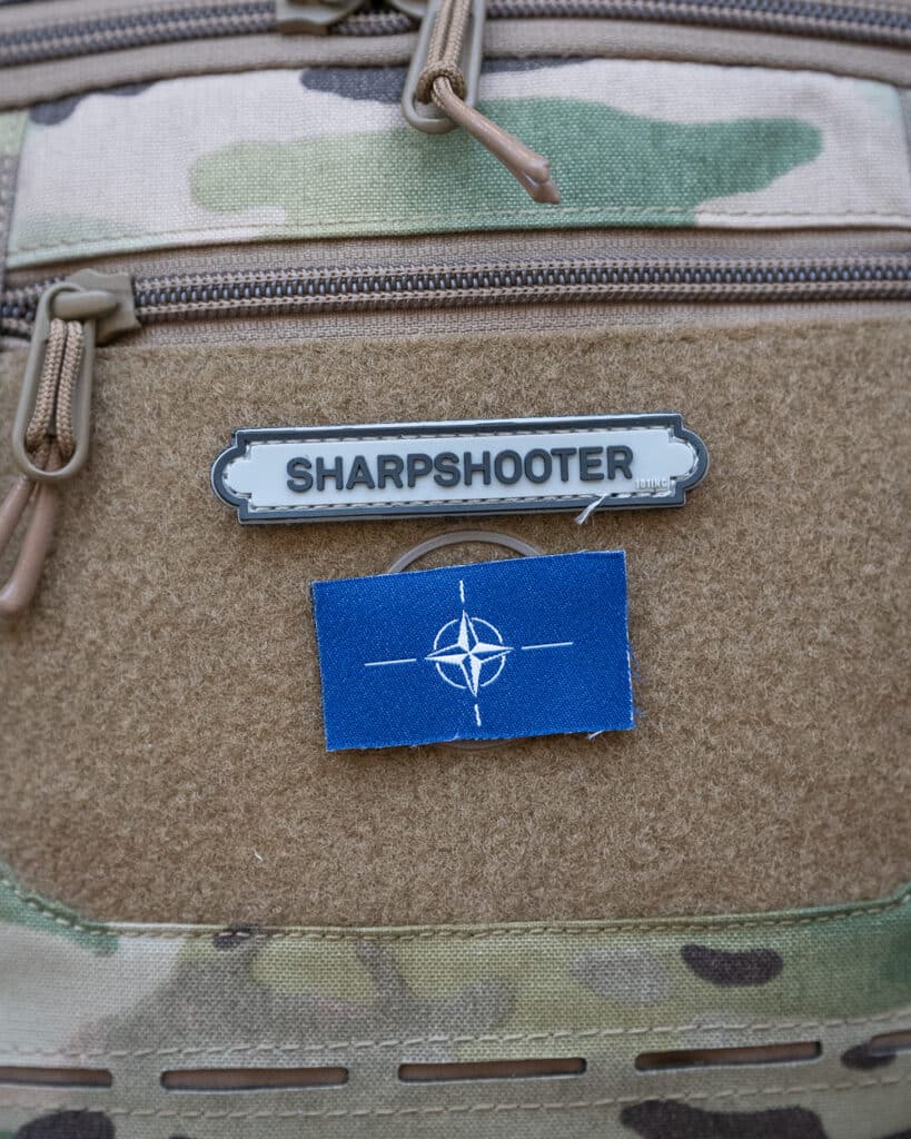 Sharpshooter Velcromerkki Harmaa, pitkulaisen muotoinen tarranauhamerkki, mustalla tekstillä "SHARPSHOOTER".